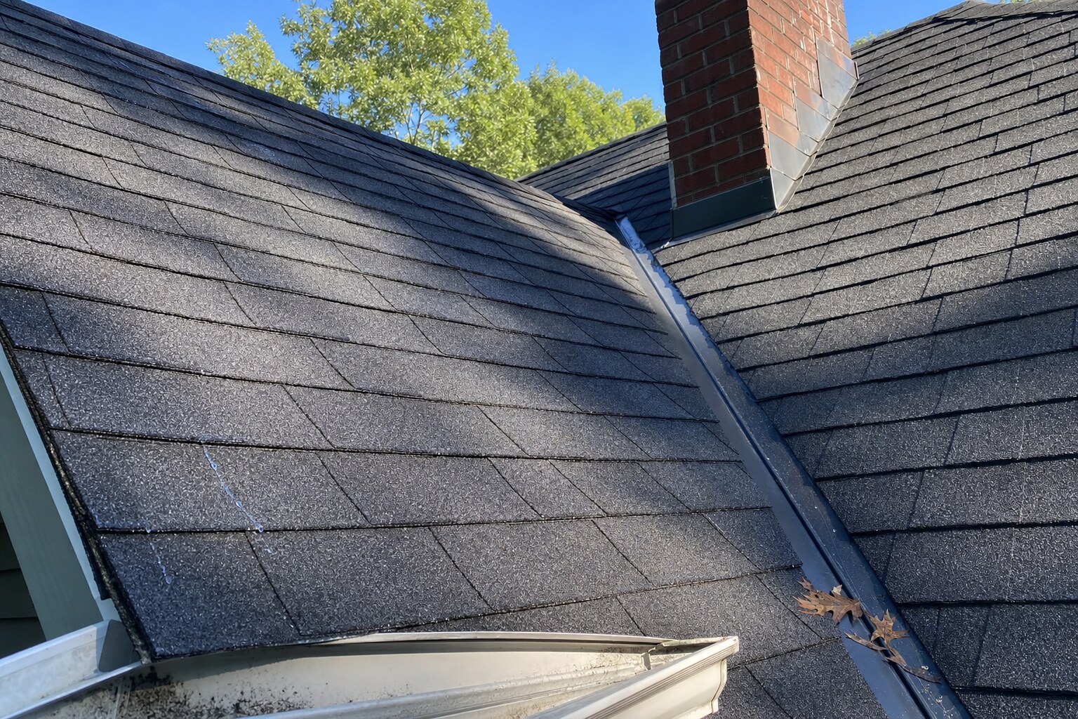 Close-up of a freshly cleaned asphalt shingle roof valley near Shavertown — chimney step-flashing and ridge cap visible